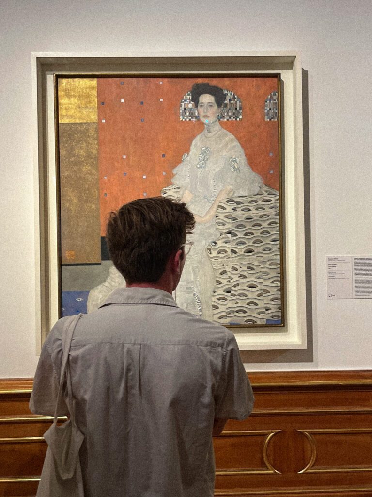 guy standing in front of gustav klimt's art in belvedere museum